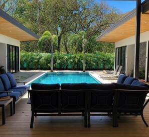Ein moderner Poolbereich im Freien mit Holzterrasse, Liegestühlen und Blick auf üppiges Grün.