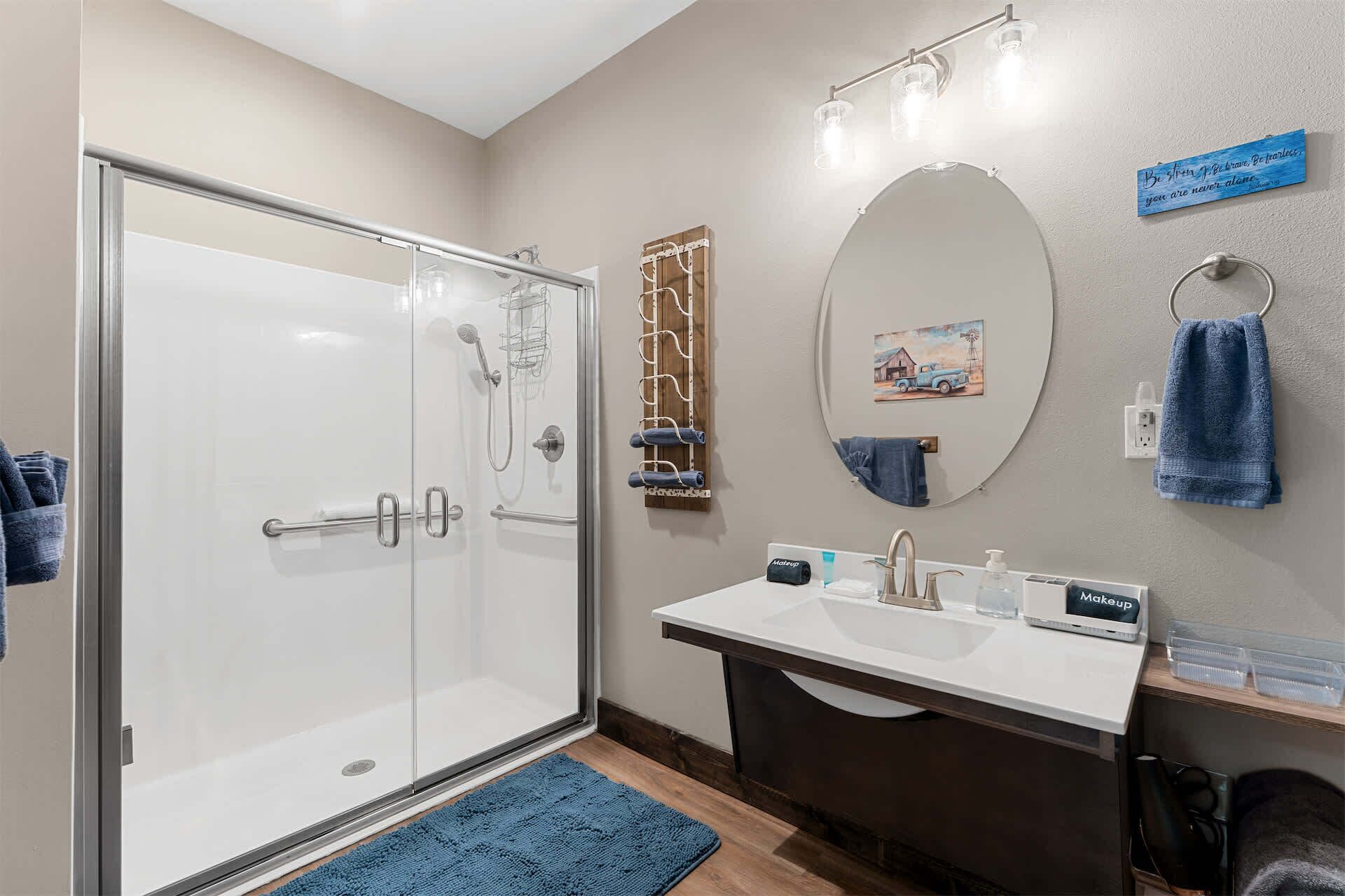 A bathroom with a glass shower enclosure, a vanity with a mirror, a towel rack, and a wall-mounted light fixture.