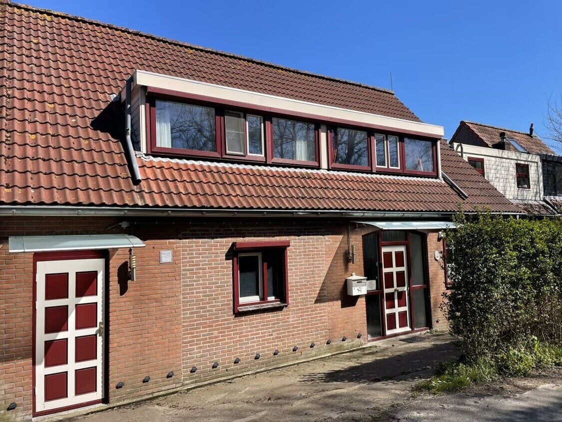 A two-story brick building with a red-tiled roof, a front door, and a small window.