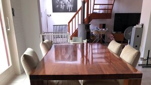 Una mesa de comedor con seis sillas, una escalera, un televisor y un ventilador en una sala de estar moderna.