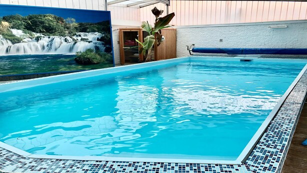 Una piscina con agua azul cristalina, rodeada por un solado de baldosas y un mural de cascada.