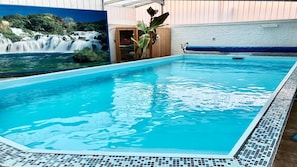 A swimming pool with clear blue water, surrounded by a tiled deck and a mural of a waterfall.