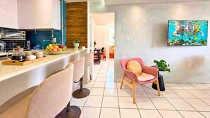 Eine moderne Küche mit Barbereich, einem Essbereich mit Stühlen und einem an der Wand befestigten Fernseher.