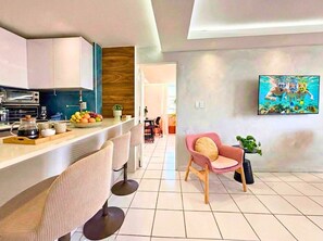 A modern kitchen with a bar area, a dining space with chairs, and a wall-mounted TV. - Ocean View! 2 Beds 2 Baths Perfect Location! - Near Beach! (San Juan)