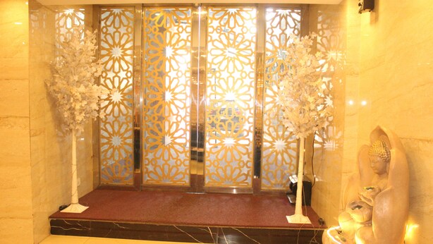 Un área de recepción con suelo de mármol, alfombra roja y una pared decorativa con diseños intrincados.