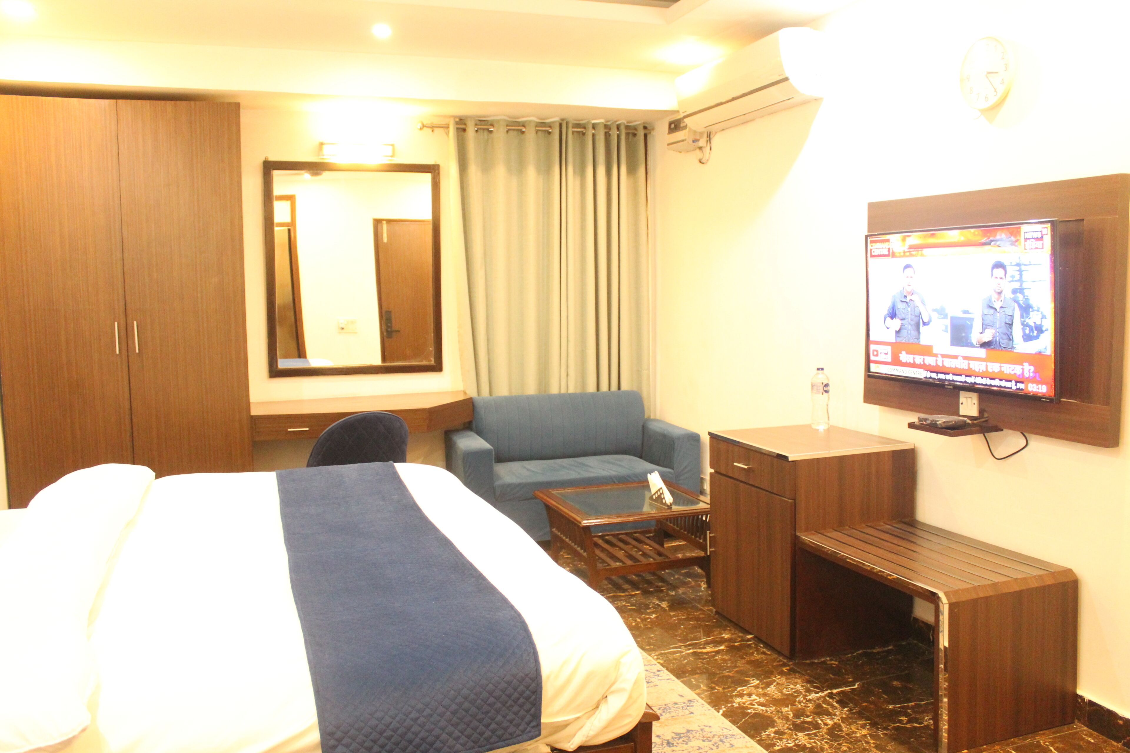 A hotel room with a bed, a sofa, a desk, a television, and a mirror.