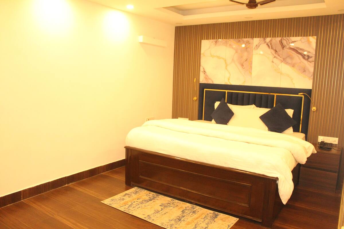 A bedroom with a bed, wooden floor, a ceiling fan, and a marble-patterned wall.