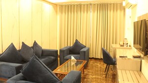 Habitación de hotel con zona de estar, sofás, una mesa de centro, televisión y un escritorio con silla.