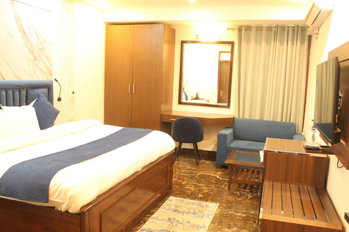 A hotel room with a bed, a desk, a chair, a sofa, a TV, and a wardrobe.