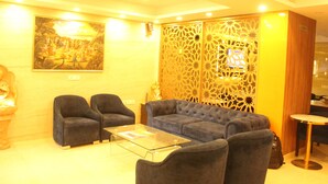 Un hall de hotel con un sofá, sillas, una mesa de centro de vidrio, un biombo decorativo y un cuadro en la pared.