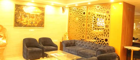 Eine Hotelhalle mit einer Couch, Sesseln, einem Glastisch, einem dekorativen Raumteiler und einem Gemälde an der Wand.