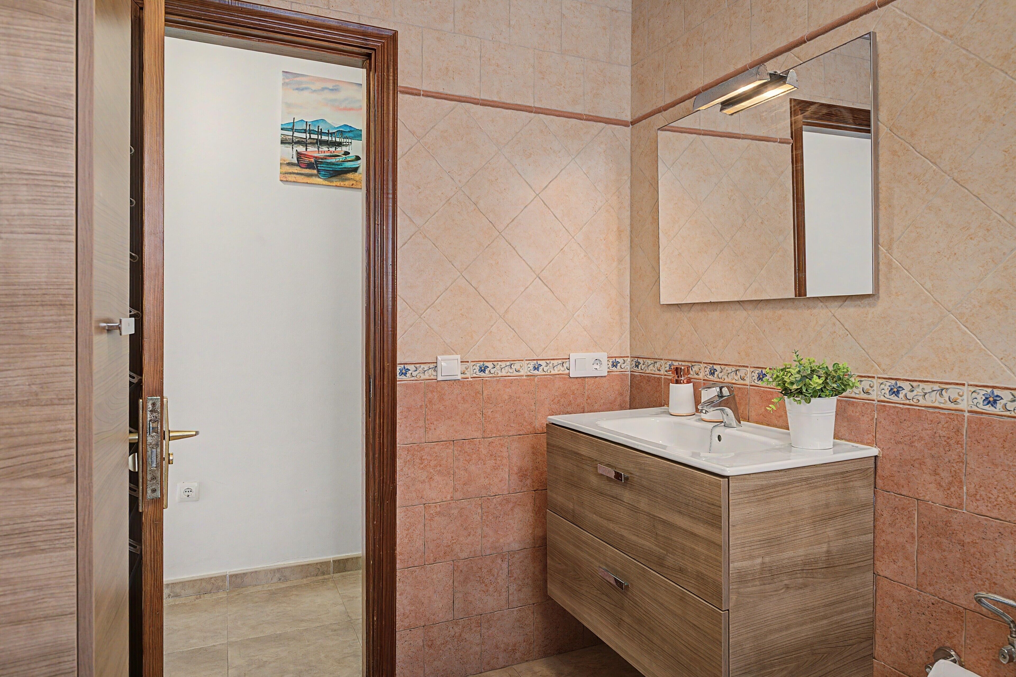 A bathroom with a wooden vanity, a mirror, a sink, and a potted plant.