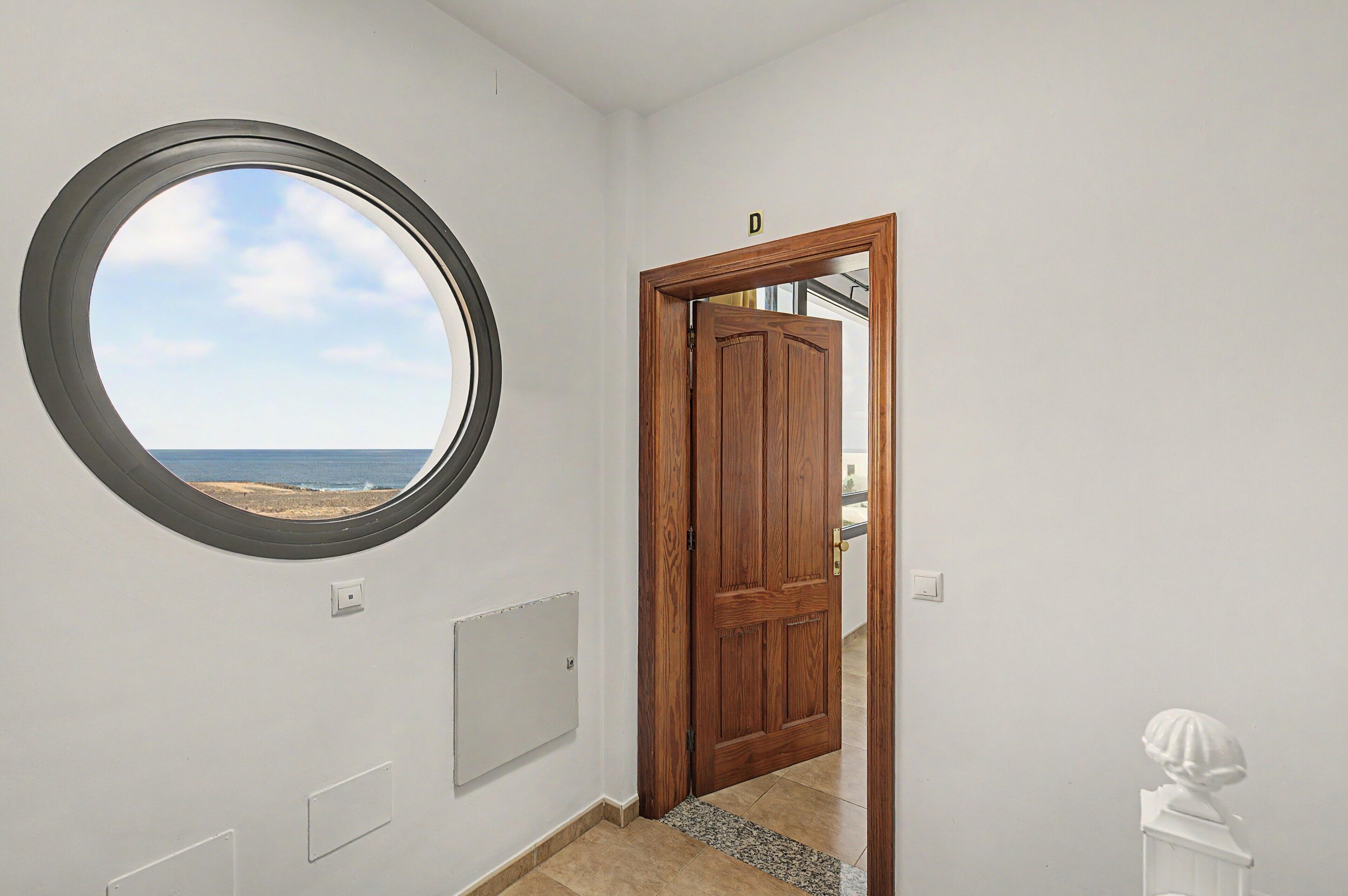 Een kamer met een rond raam, een houten deur en uitzicht op het strand.