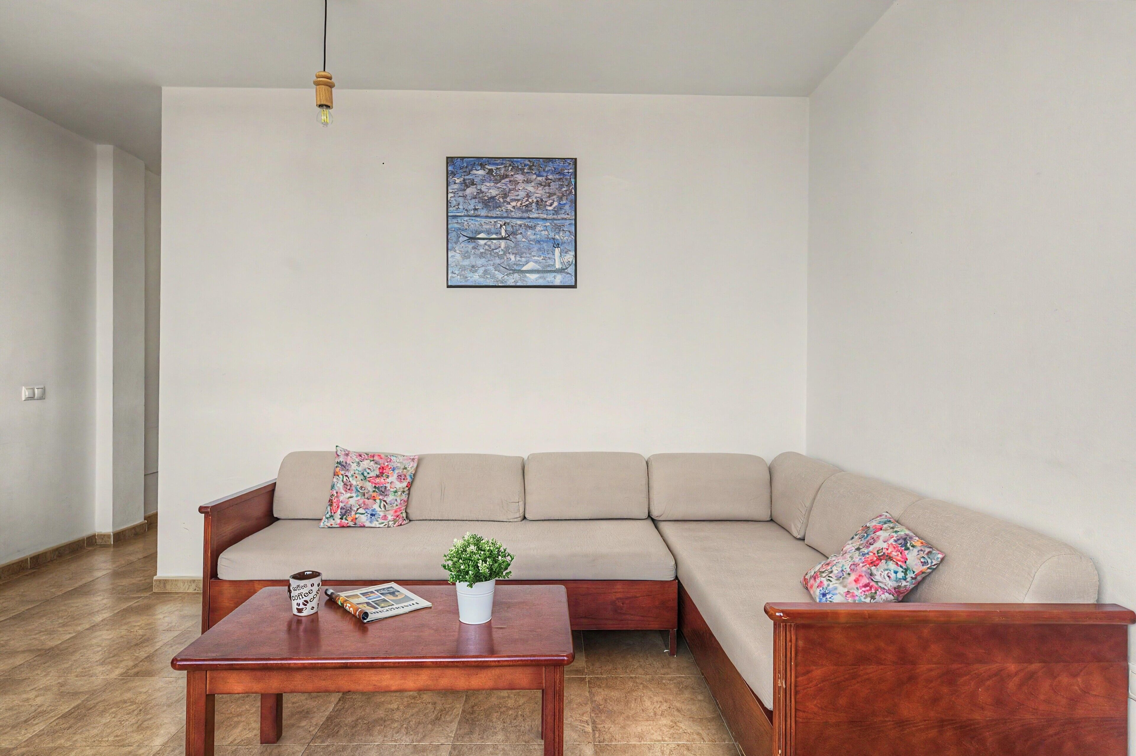 Una sala de estar con un sofá color beige, una mesa de centro de madera, una pequeña planta en maceta y una obra de arte enmarcada en la pared.