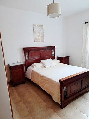 A bedroom with a wooden bed, a bedside table, a nightstand, a hanging light fixture, and a wall-mounted picture. - Vacation Apartment 'La Caracola' with Sea View and Wi-Fi (La Santa)