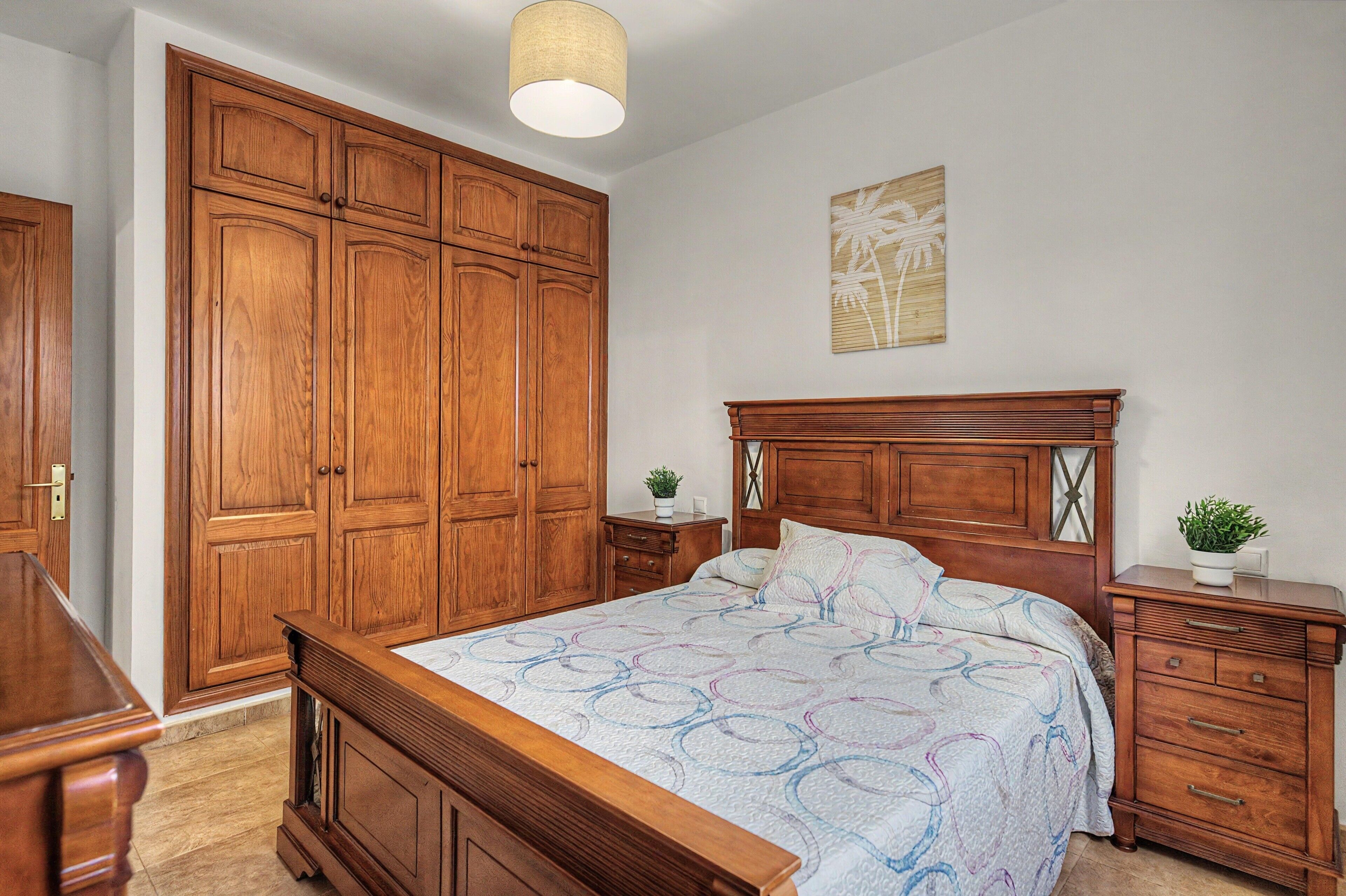 A bedroom with a wooden bed, a nightstand, a dresser, and a large wardrobe.