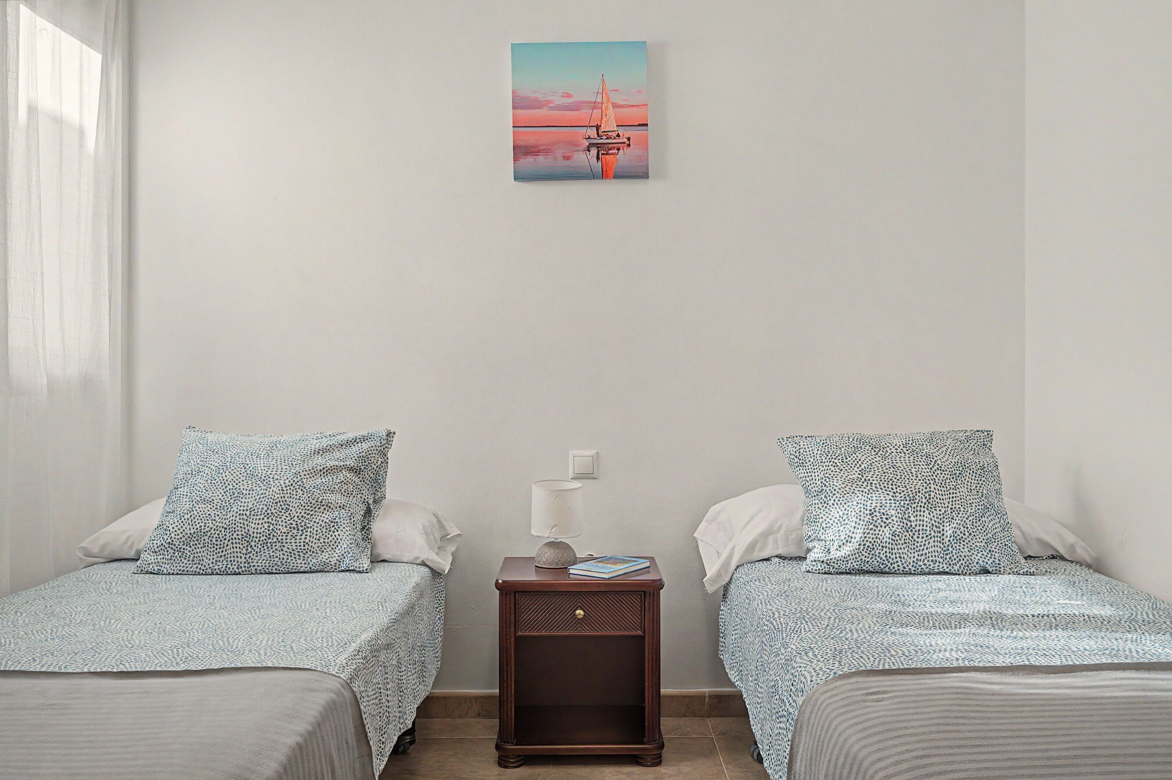 Una habitación con dos camas individuales, una mesita de noche con lámpara y un cuadro en la pared.