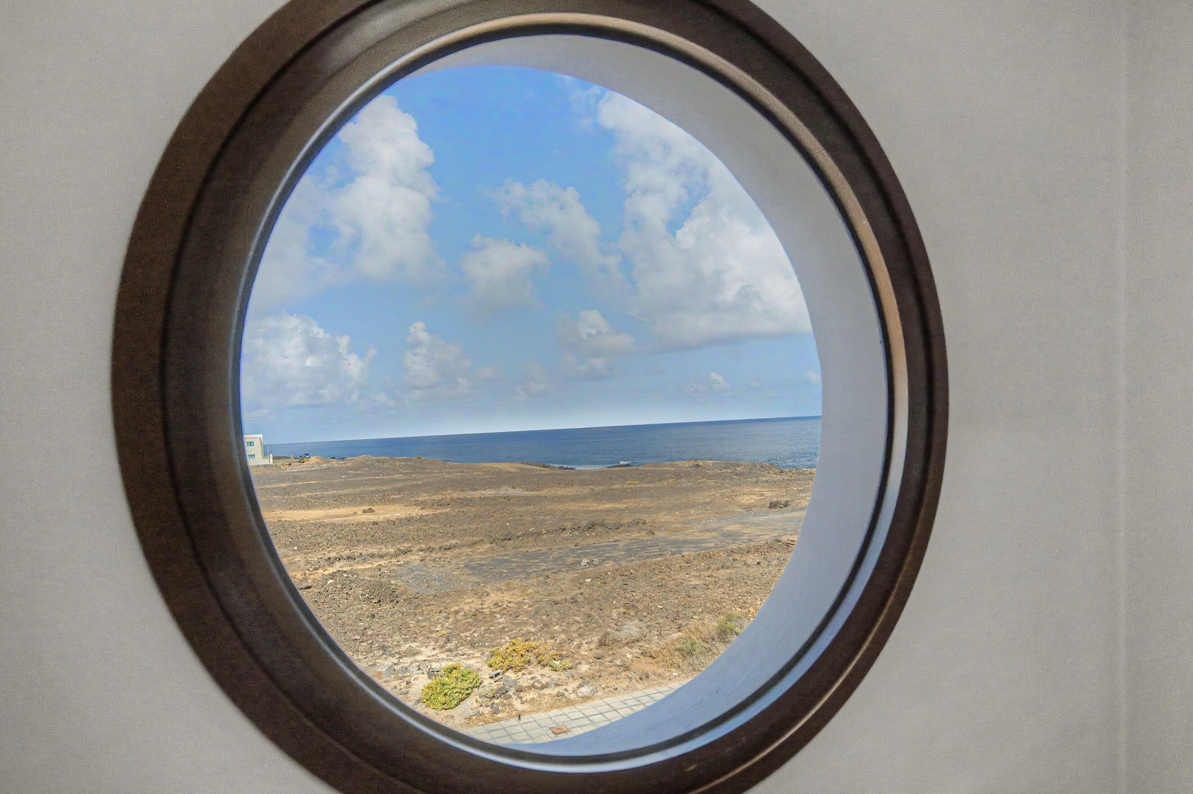 A round window with a view of a barren landscape, a clear sky, and a distant horizon.