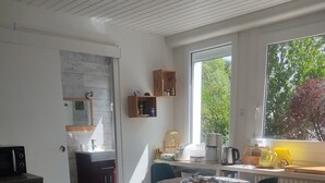 A modern kitchen with a built-in oven, a dining area with a round table and chairs, and a large window with a view of trees. - Unique bed-and-breakfast, charming vacation rental, countryside, beach 15 minutes away (Saint-Malo-de-Guersac)