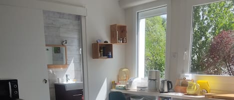 Una cocina moderna con horno empotrado, un comedor con mesa redonda y sillas, y un ventanal con vistas a árboles.
