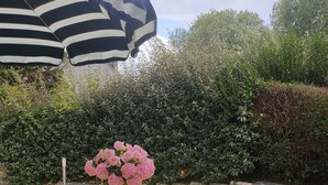 A table set outdoors with a bright yellow tablecloth, white chairs, a striped umbrella, and a vase of pink flowers. - Unique bed-and-breakfast, charming vacation rental, countryside, beach 15 minutes away (Saint-Malo-de-Guersac)