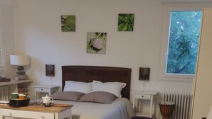 A bedroom with a bed, bedside tables, a chair, a round table, a wicker chair, and a window with a view of trees. - Unique bed-and-breakfast, charming vacation rental, countryside, beach 15 minutes away (Saint-Malo-de-Guersac)