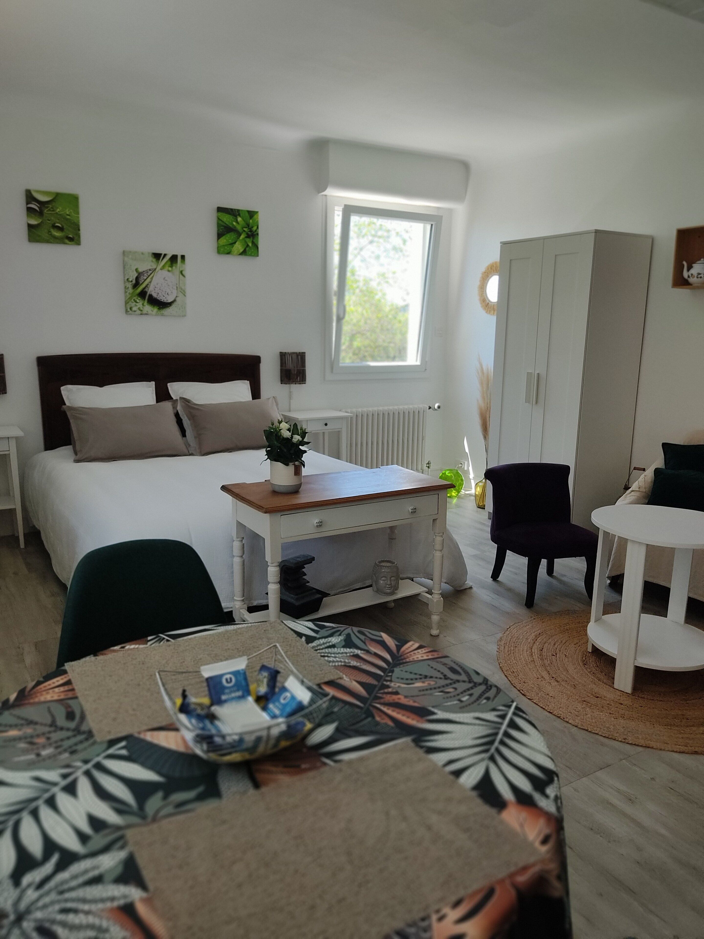 Un dormitorio con cama, mesita de noche, silla y una pequeña mesa con una planta.