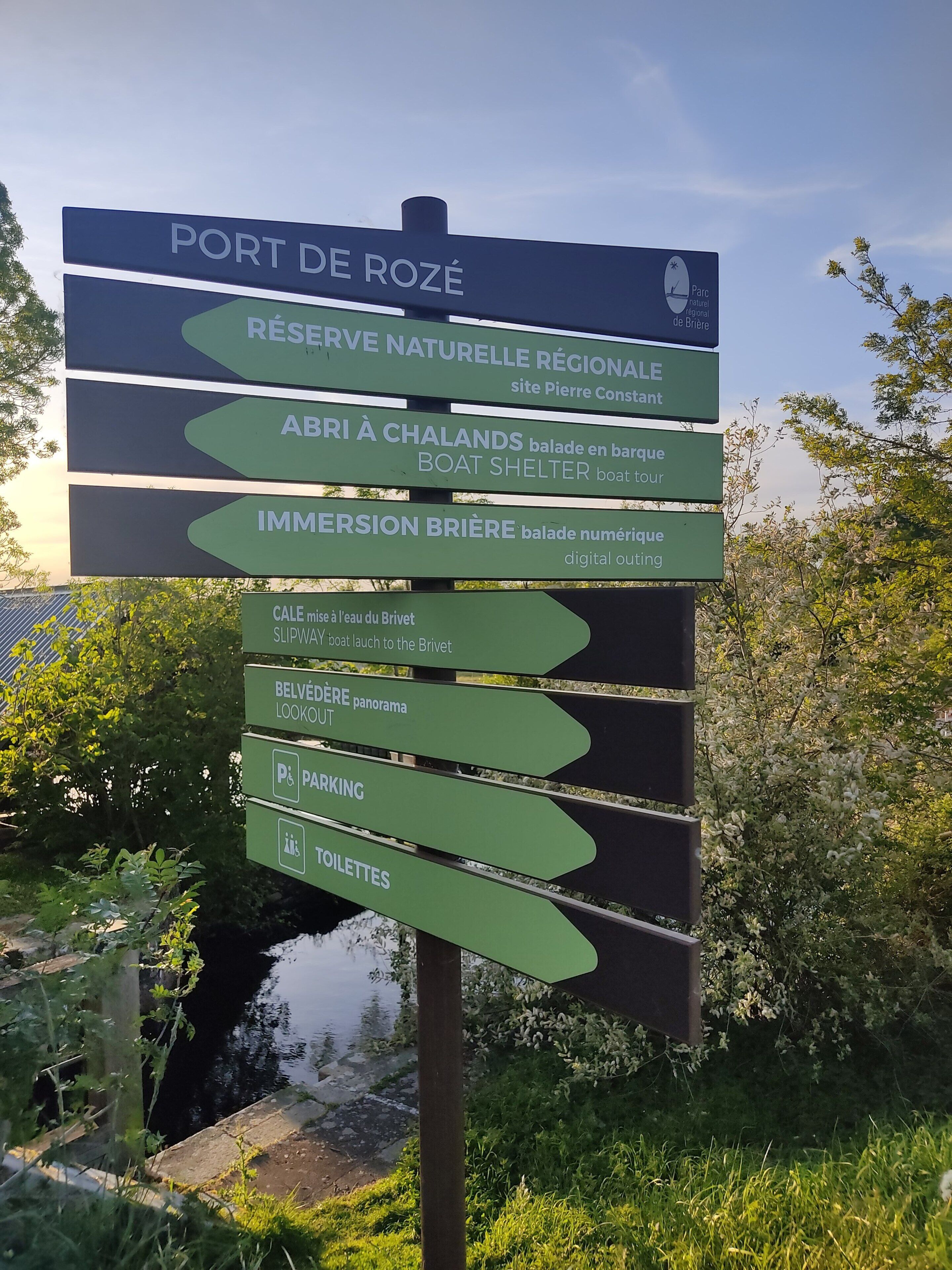 A directional sign with multiple green arrows pointing to various amenities such as a natural reserve, boat shelter, and parking.