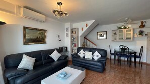 A living room with two black leather sofas, a white coffee table, a dining area with a table and chairs, and a staircase. - Terrasol Isis D Plex A 1 Minuto DE LA Playa (Velez-Malaga)