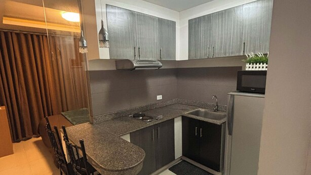 A compact kitchen with a dining area, a microwave, and a refrigerator. - Cozy 1-bedroom condo in perfect Manila with AC pool and fitness (Manila)
