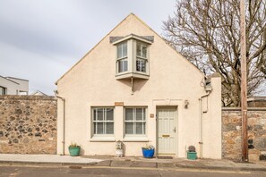 A building with a pitched roof, a bay window, a door, and two potted plants.