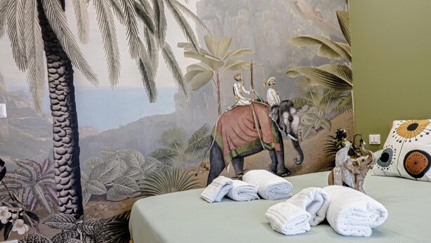 Une chambre ornée d’une fresque représentant un éléphant et son cavalier, un lit avec des serviettes soigneusement pliées, et une statue d’éléphant décorative.
