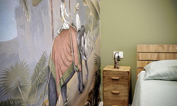 Una camera da letto con un affresco, un comodino in legno con una lampada e un letto.