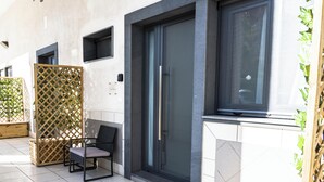Une façade moderne avec une grande porte vitrée, un paravent en treillis de bois et une chaise à l’extérieur.