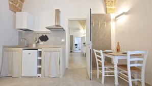 Een kleine keuken met een geïntegreerde koelkast, een fornuis en een eethoek met een tafel en stoelen.