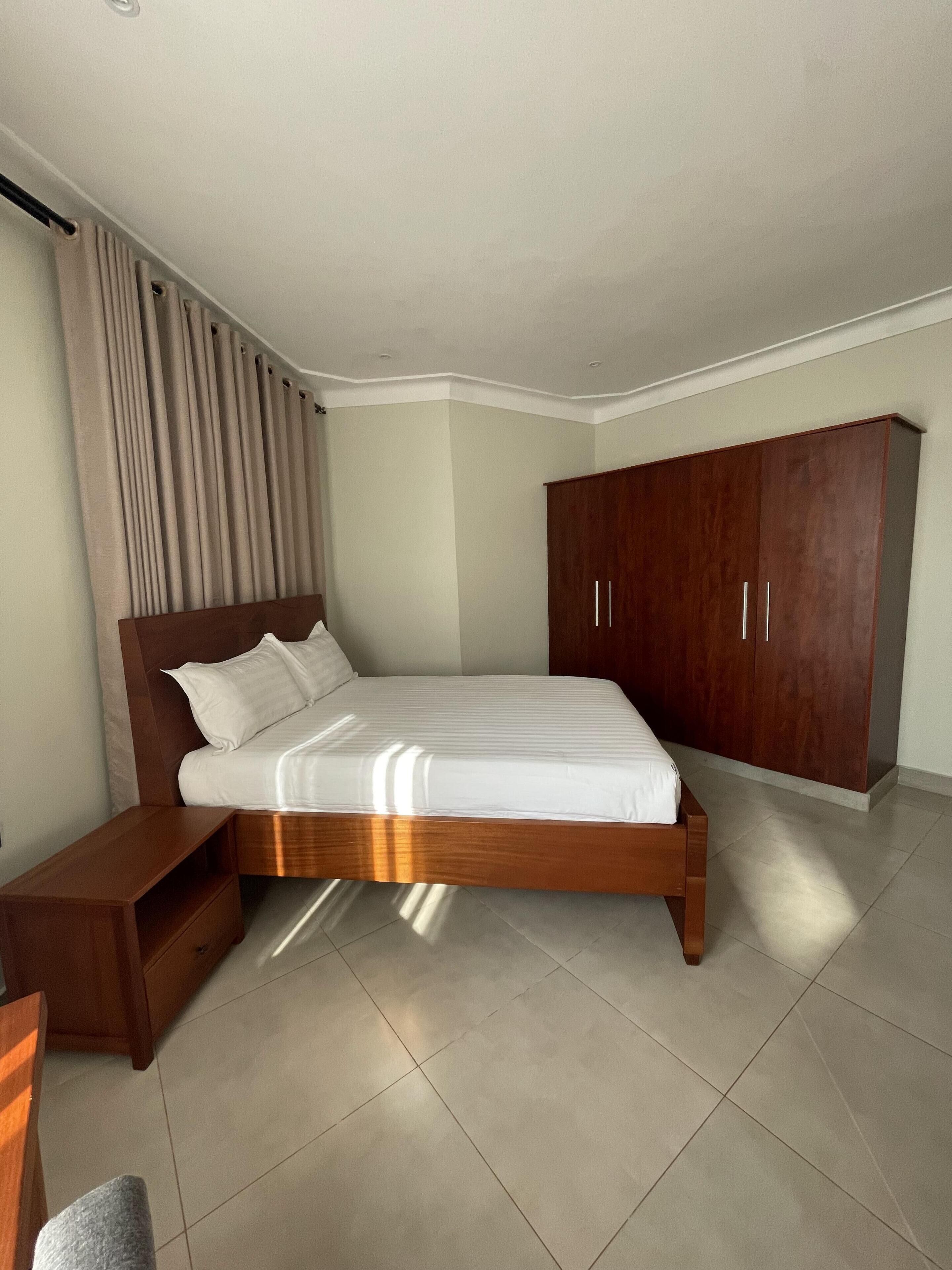 A modern bedroom with a wooden bed, a nightstand, a wardrobe, and a large window with curtains.