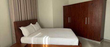 A modern bedroom with a wooden bed, a nightstand, a wardrobe, and a large window with curtains.