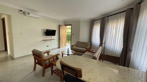 Una sala de estar moderna con una mesa de comedor, sillas de madera, un televisor de pantalla plana y un ventanal con cortinas.