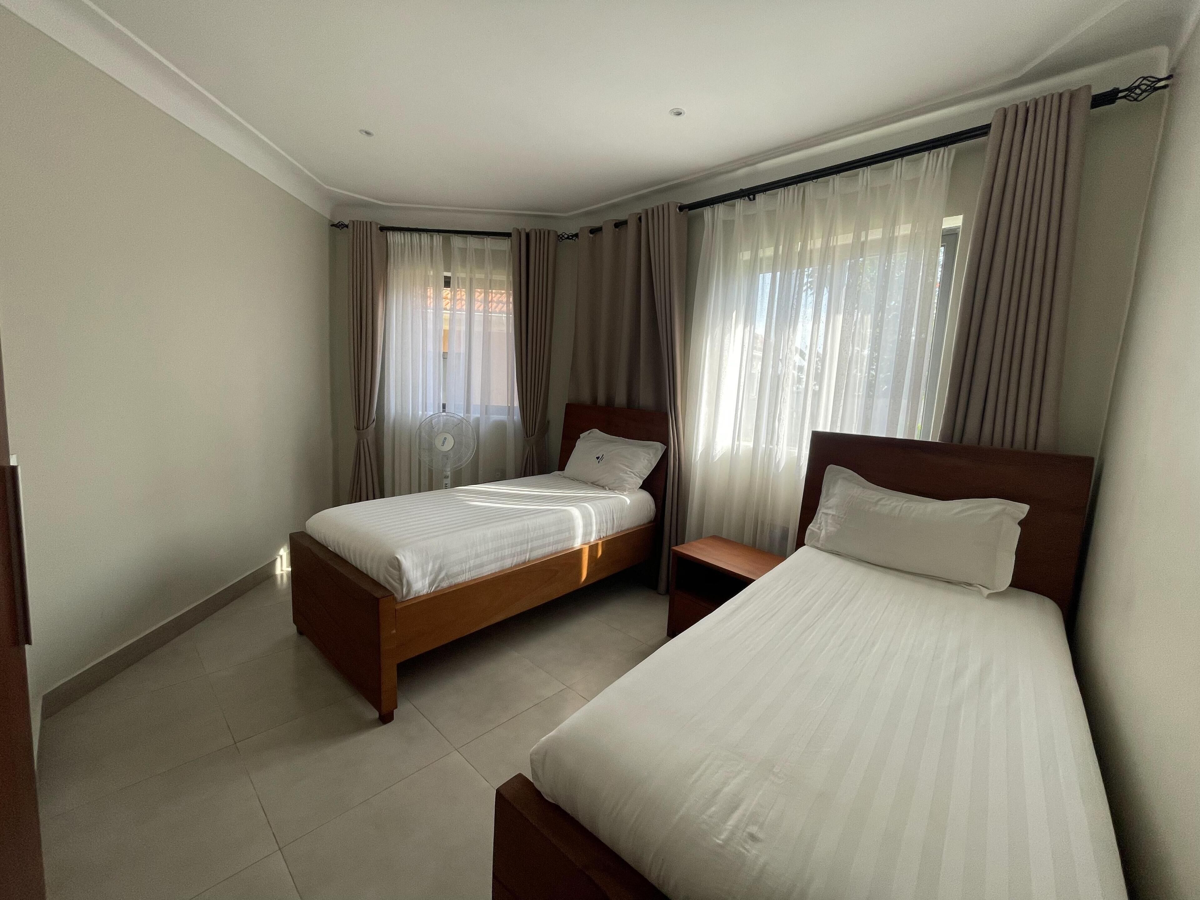 Ein Hotelzimmer mit zwei Betten, einem Nachttisch, einem Ventilator und Vorhängen.