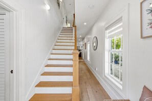 A staircase with wooden steps and white walls, leading to a room with a large window and a door. - Mermaids Cove - Luxury Meets Location - 5BD/5.5Bath, May - August 10% off (Key West)