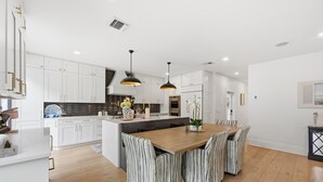 A modern kitchen with white cabinets, a wooden dining table, and striped chairs. - Mermaids Cove - Luxury Meets Location - 5BD/5.5Bath (Key West)