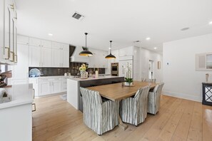 A modern kitchen with white cabinets, a wooden dining table, and striped chairs. - Mermaids Cove - Luxury Meets Location - 5BD/5.5Bath, May - August 10% off (Key West)