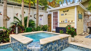 A swimming pool with a tiled edge, surrounded by plants and a building with a sign reading 'TIKI BAR'. - Mermaids Cove - Luxury Meets Location - 5BD/5.5Bath (Key West)