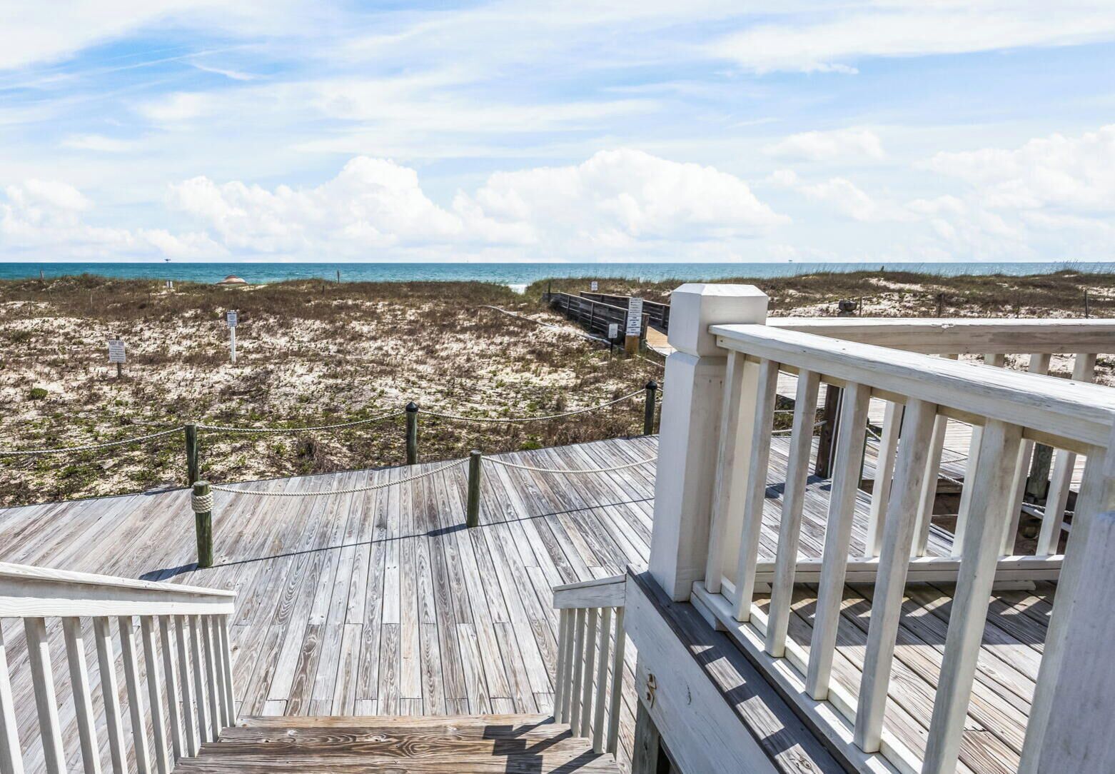 Une terrasse en bois avec une rambarde donnant sur une plage.