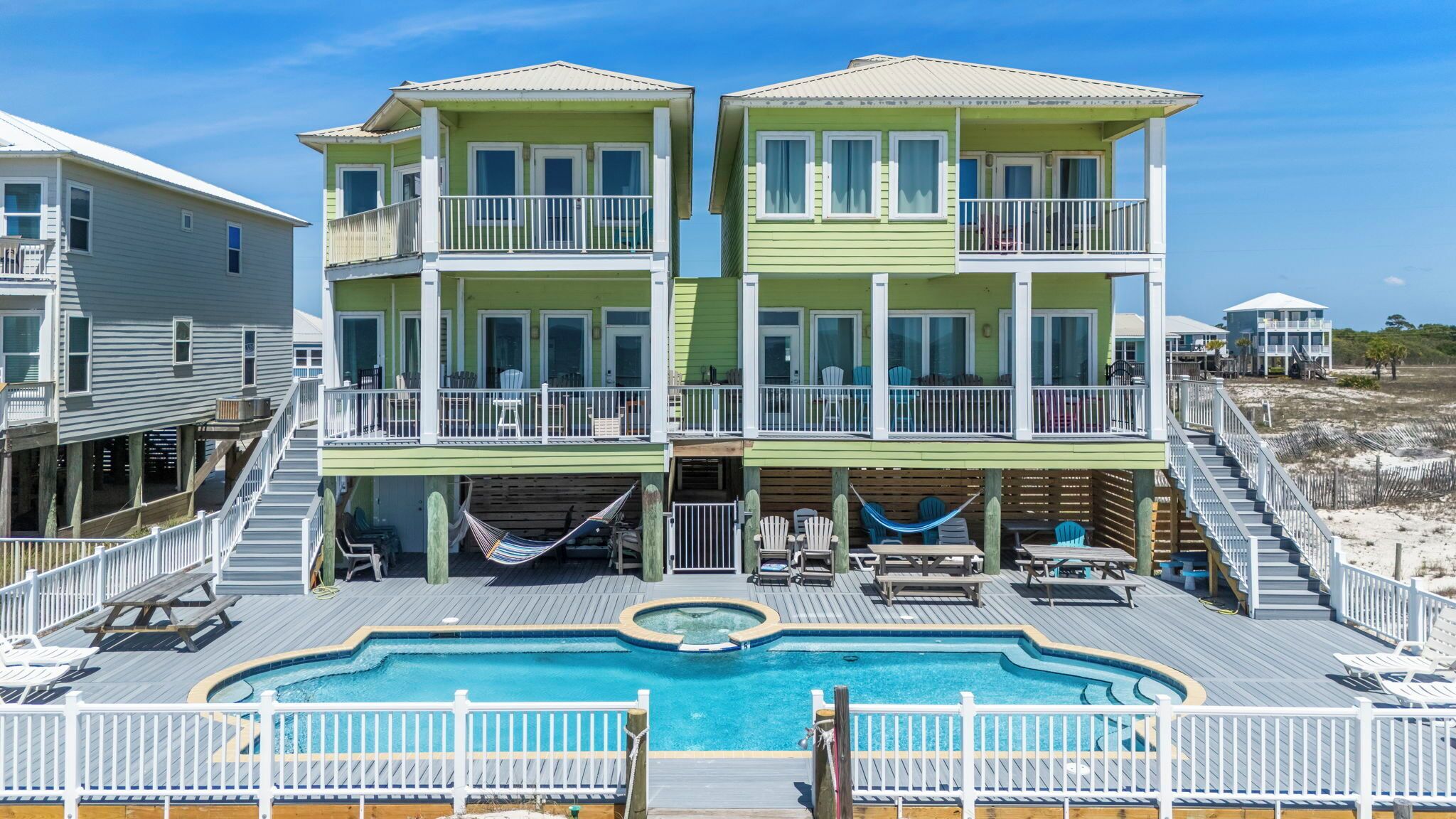 Ein Strandhaus mit zwei Etagen, einem Swimmingpool, Sitzmöglichkeiten im Freien und einer Whirlwanne.