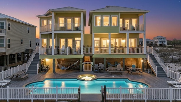 Una casa frente a la playa de dos pisos con piscina, sillas de deck y jacuzzi.