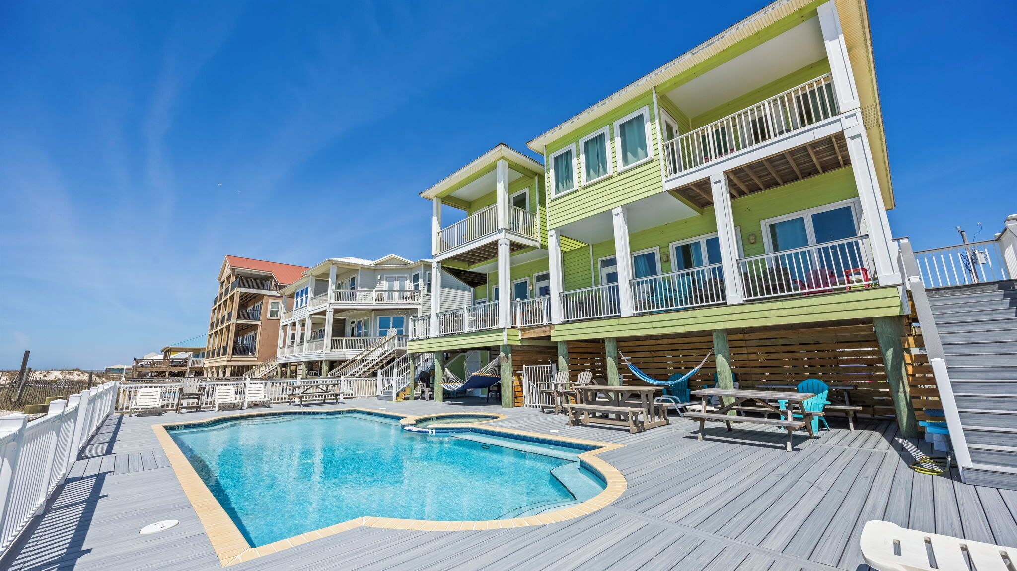A multi-story hotel with a pool area, outdoor seating, and a view of the beach.