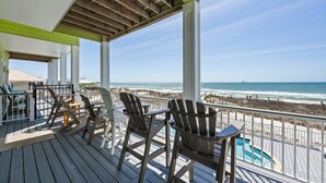 Una terraza de madera con sillas y una piscina, con vista a una playa y una cerca de madera.