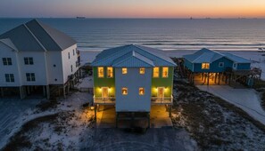 Ein Strandgrundstück mit mehreren Häusern, darunter ein auffälliges, grünes Haus mit Balkon sowie ein weißes Haus mit überdachter Veranda.