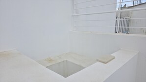 Ein Zimmer mit weißem Boden, einem kleinen quadratischen Fenster und einem weißen Geländer.